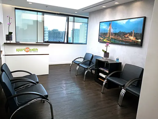 Imagem de uma sala de espera com cadeiras, uma janela e com a logo do Sports Health no balcão de atendimento.